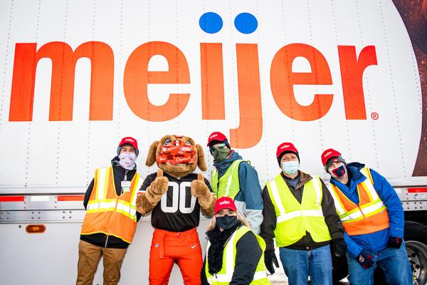 Meijer team members wearing face masks and reflective vests stand in front of a Meijer delivery truck with the Cleveland Browns mascot giving a thumbs up.