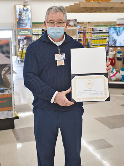 John Spaulding poses proudly in the pets department of his store holding his Fred Meijer Award certificate. 