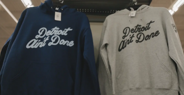 Navy and grey sweatshirts that read “Detroit Ain’t Done” in a bold cursive font hang on a rack with price tags.