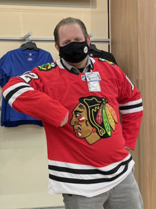 Todd Bevering stands wearing a black face mask and red hockey jersey with the Blackhawks logo on it.