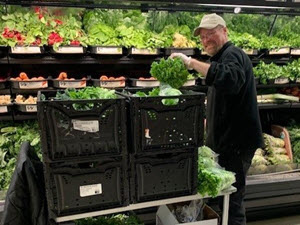Meijer team member loads kale from a recycled plastic container onto the shelf.