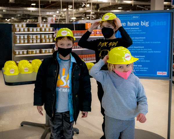 Children smile in Meijer hard hats at front entrance of store.