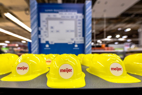 Plastic Meijer hard hats sit on a table in front of a sign explaining the store’s remodel.