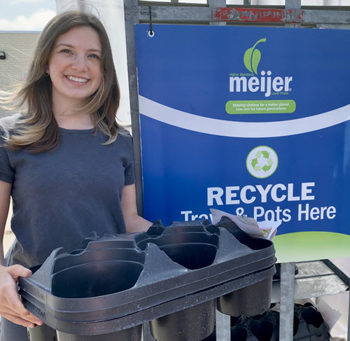 Annalise Steketee holds plastic trays next to recycling cart sign.
