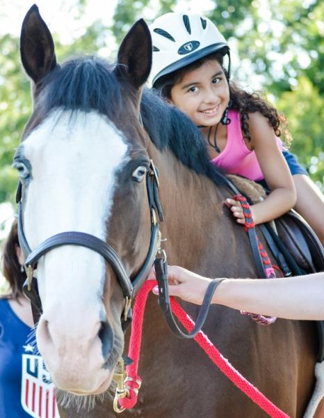 A young girl in a helmet sits on a horse being guided by Cheff Center staff.