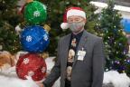 Cedar Springs Store Director Larry Levin, dressed in Santa hat by holiday display of trees and ornaments