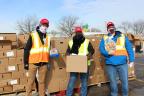 Meijer team members wearing face masks and reflective vests stand holding turkeys in front of hundreds of boxes of turkeys.