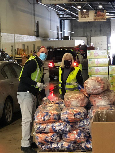 Two Meijer team members wear masks and reflective vests in a warehouse next to dozens of large bags of food