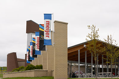 Columns outside of an outdoor pavilion have display alternating signs displaying the logos of Meijer and the West Michigan Sports Commission. 