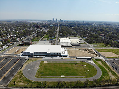 An aerial view of the sports complex shows the new building and outdoor track near industrial buildings and neighborhoods with the Louisville skyline in the distance.