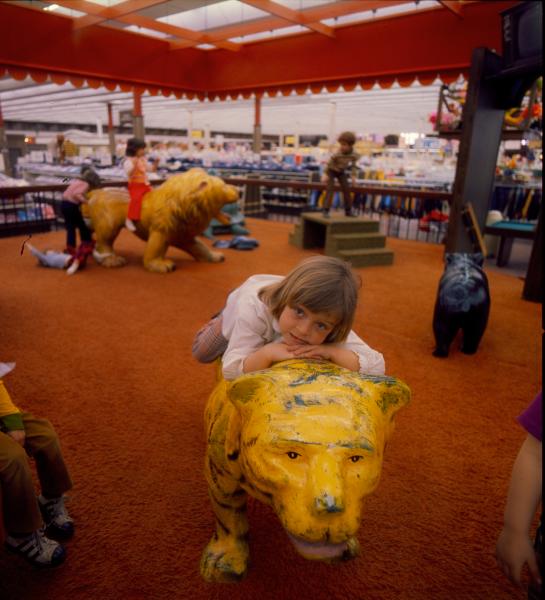 Child laying on lion statue as kids play nearby at historic West Saginaw Meijer playland 