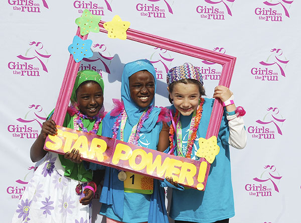 Young girls stand close together smiling at a Girls on the Run event.