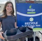 Annalise Steketee holds plastic trays next to recycling cart sign.