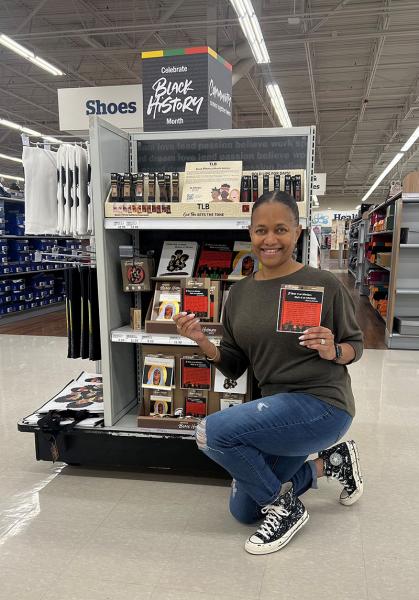 Dana holding a sticker and magnet featuring her art in a Meijer store in front of a display highlighting the Black History Month artist collection 