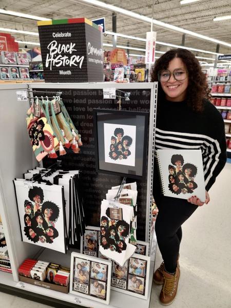 Melina holding a notebook featuring her art in a Meijer store in front of a display highlighting the Black History Month artist collection 