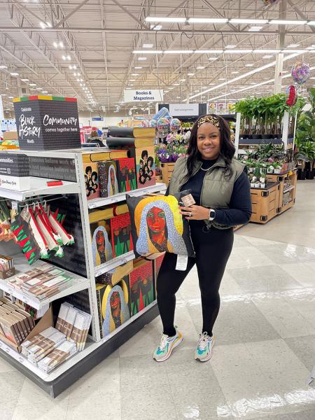 Shaunt’e Lewis holding a pillow featuring her art in a Meijer store in front of a display highlighting the Black History Month artist collection 